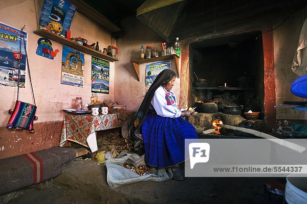 Eine Hausfrau an der Feuerstelle in ihrer Küche  sie trägt die tradtionelle Kleidung der Amantani-Quechua  Isla Amantani im Titicaca-See  Amantani  Peru  Südamerika