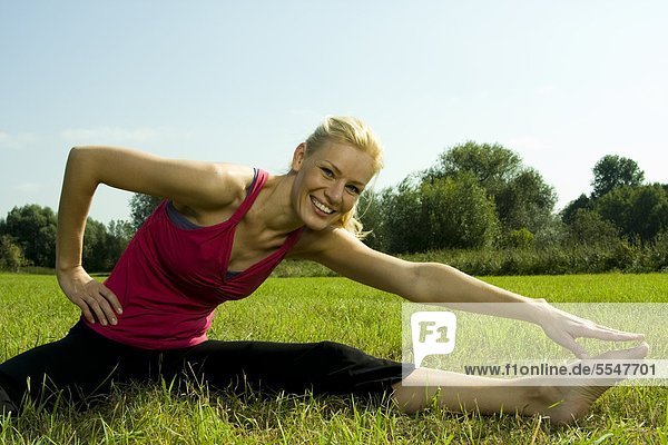 Young woman stretching in meadow