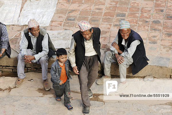 Männer mit traditioneller Kopfbedeckung und Junge auf dem Taumadhi-Platz Bhaktapur Kathmandu-Tal Nepal Asien