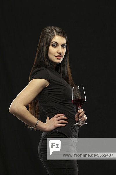 Junge Frau in Abendkleid hält ein Glas Rotwein