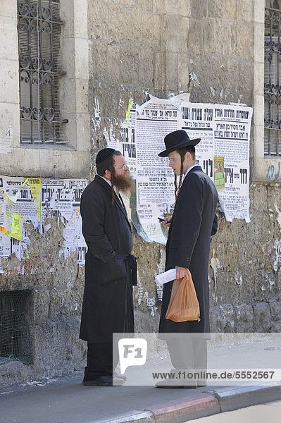 Orthodox Jews having a conversation in front of wall newspapers in the district of Me'a She'arim or Mea Shearim  Jerusalem  Israel  Middle East