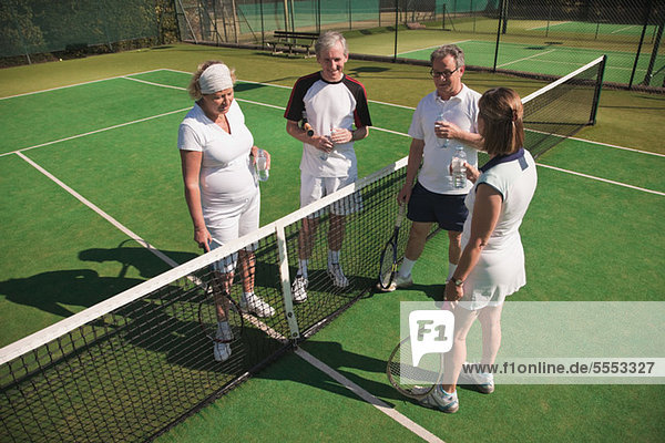 Senior and mature adults enjoying drink on tennis court