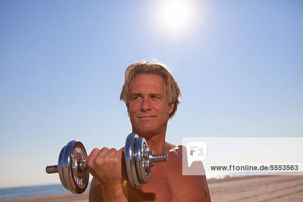 Bare-chested man on beach with dumbbell