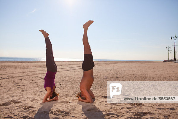 Woman and man performing handstands on beach