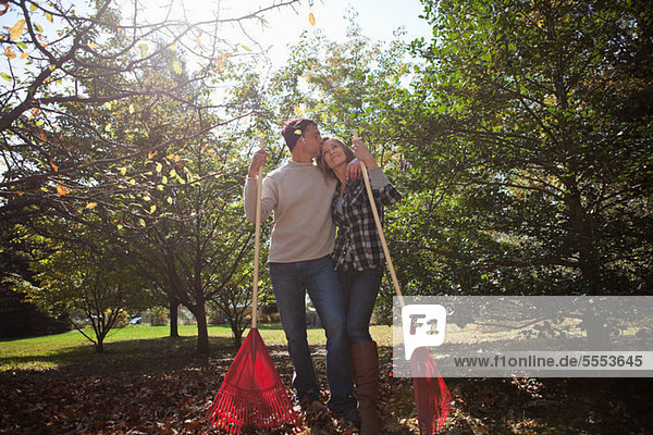 Affectionate couple with leaf rakes