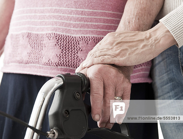 Frau berührt die Hand einer alten Frau mit Rollator