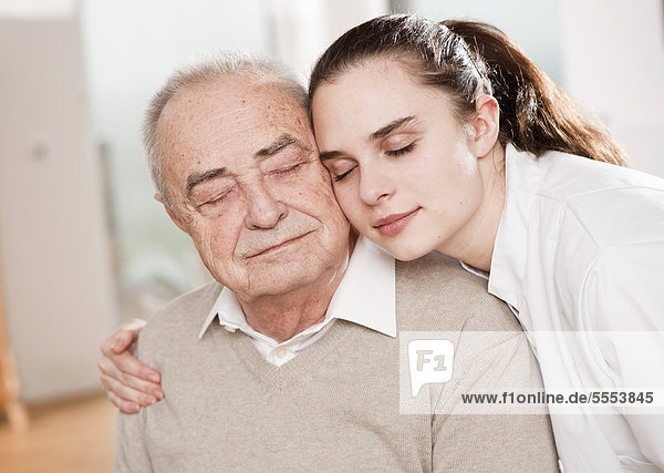 Junge Frau im Arztkittel umarmt Senior