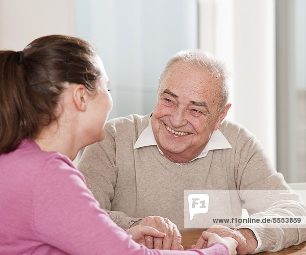 Junge Frau und Senior sitzen Hand in Hand am Tisch