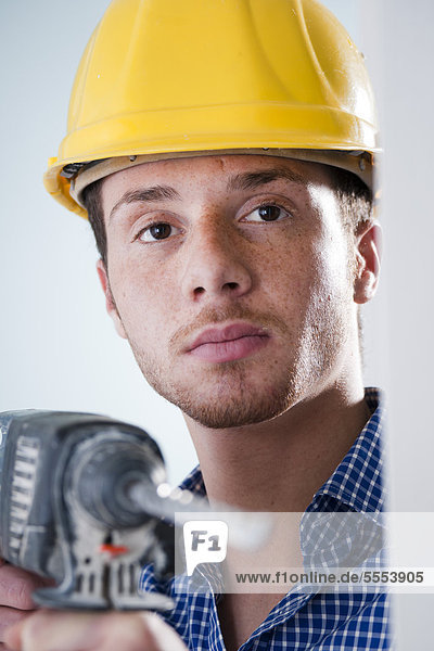 Young man wearing hard hat using drilling machine  portrait