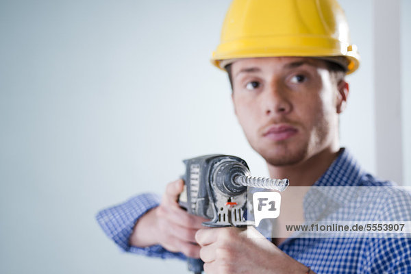 Young man wearing hard hat using drilling machine