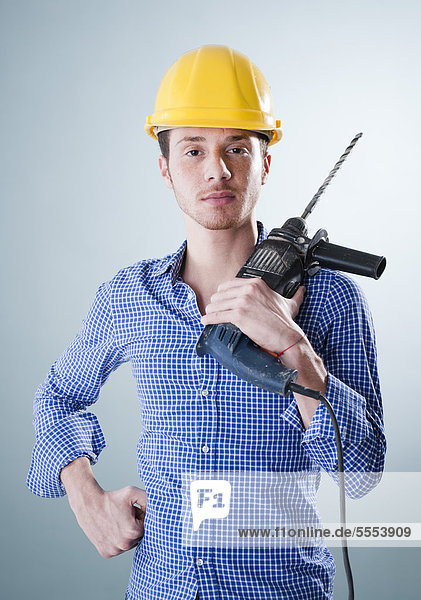 Young man wearing hard hat holding drilling machine