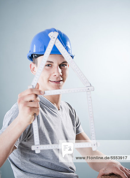 Young man wearing hard hat holding folding rule in shape of a model house