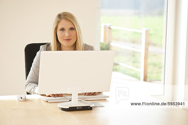Lächelnde blonde junge Frau im Büro arbeitet am Computer