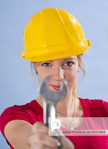 Young woman with hard hat holding wrench