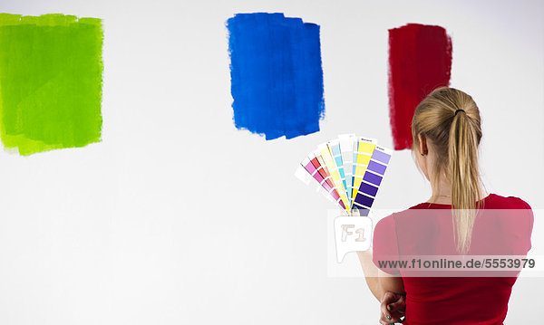 Junge Frau steht mit Farbmustern vor einer Wand
