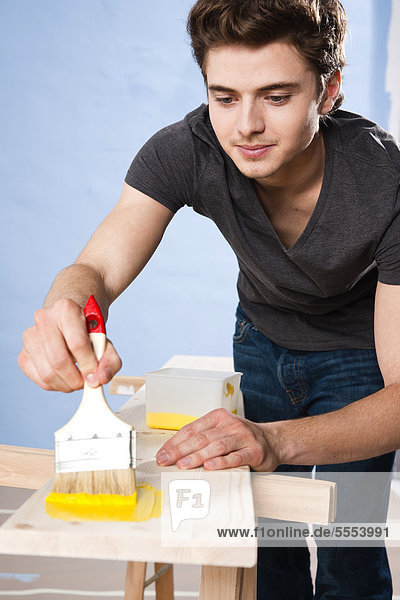 Young man painting wooden board