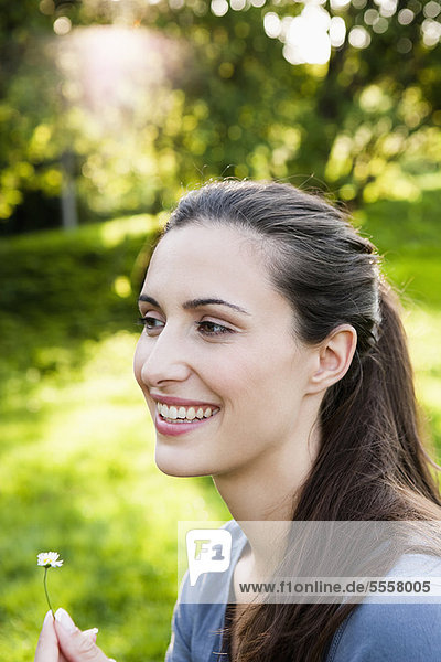 Smiling woman holding flower in park
