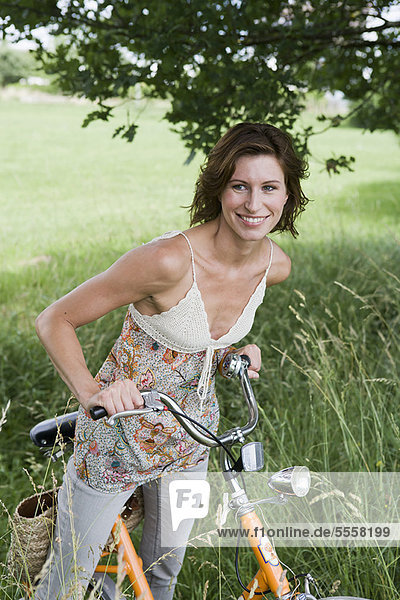 Frau schiebt Fahrrad im hohen Gras