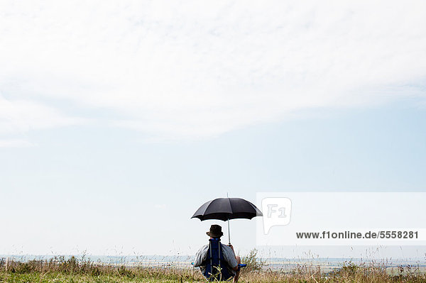 Mann sitzend unter Schirm im Feld