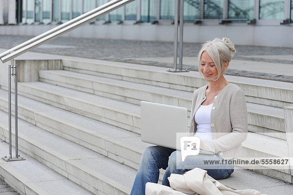 Older woman using laptop on steps