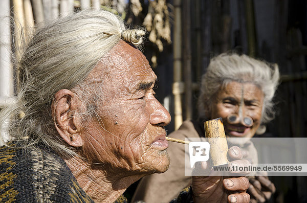 Old Apatani man with the typical hair knot at the forehead  next to a woman with the traditional noseplugs  in front of their house  Hong village  Arunachal Pradesh  India  Asia