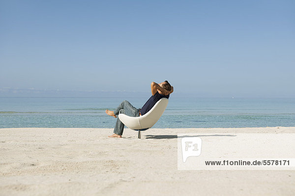 Mann im mittleren Erwachsenenalter entspannt im Sessel am Strand