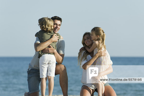 Eltern umarmen Kinder am Strand