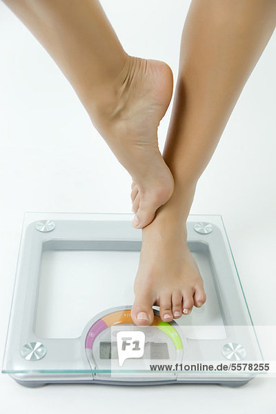 Woman standing on one leg on bathroom scale  low section