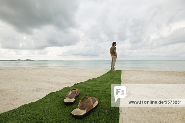 Mann steht am Ende des Teppichs am Strand  Sandalen im Vordergrund
