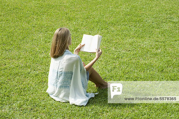 Junge Frau auf Gras sitzend Lesebuch