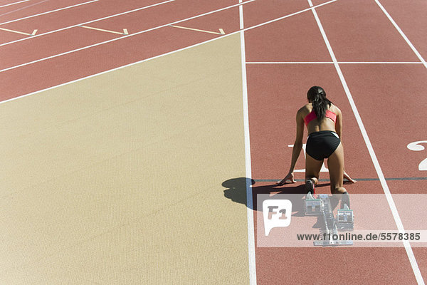 Woman crouched in starting position on running track  rear view