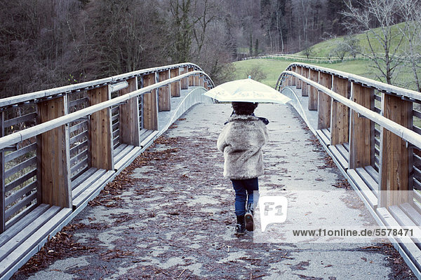 Mädchen auf Brücke mit Regenschirm  Rückansicht