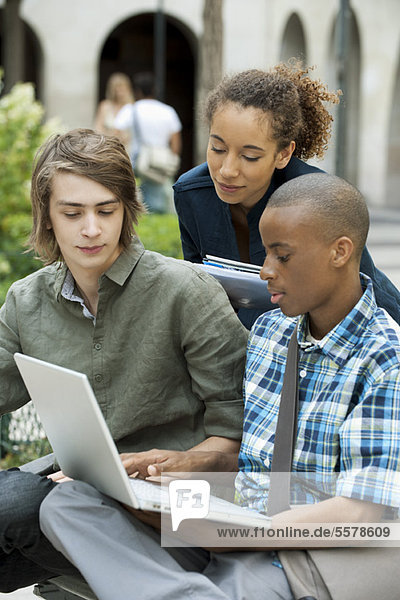 University students discussing homework on campus with laptop computer