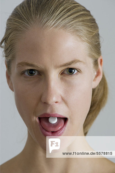 Vitaminpille auf der Zunge einer jungen Frau