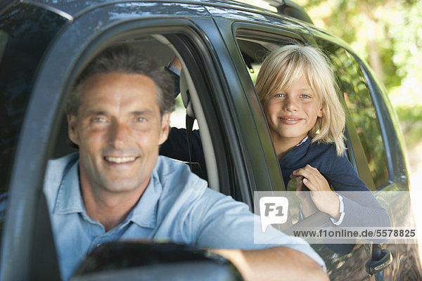 Boy riding in car with father  leaning out window and smiling at camera