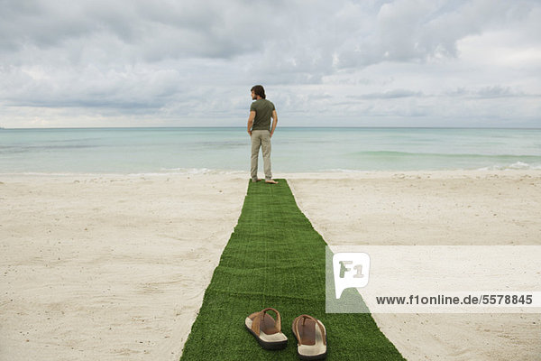 Mann steht am Ende des Teppichs am Strand  Sandalen im Vordergrund