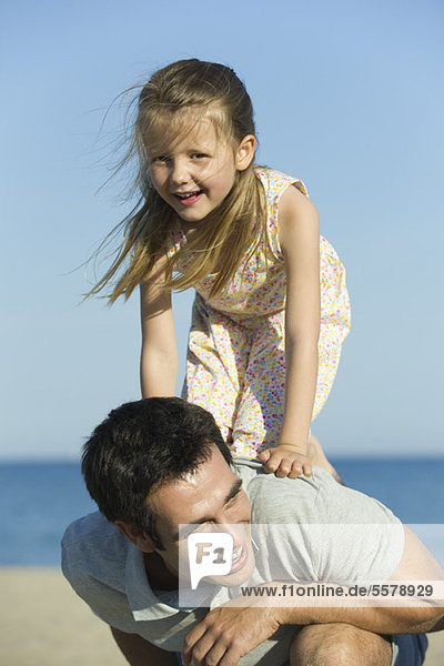 Kleines Mädchen  das auf dem Rücken seines Vaters balanciert.