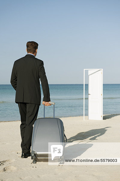 Geschäftsmann zieht Koffer am Strand  halboffene Tür im Hintergrund