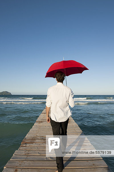 Mann auf Pier mit rotem Regenschirm  Rückansicht