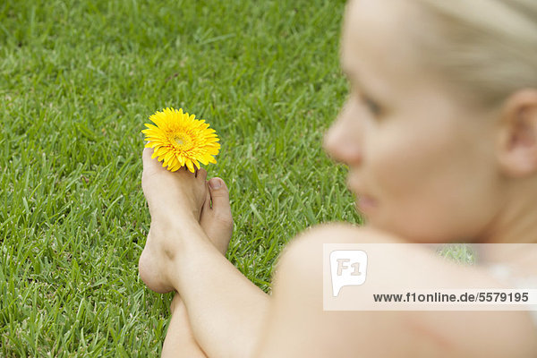 Woman holding flower between toes  looking away
