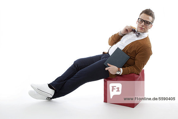 Junger Mann mit Brille und Fliege auf Sitzwürfel