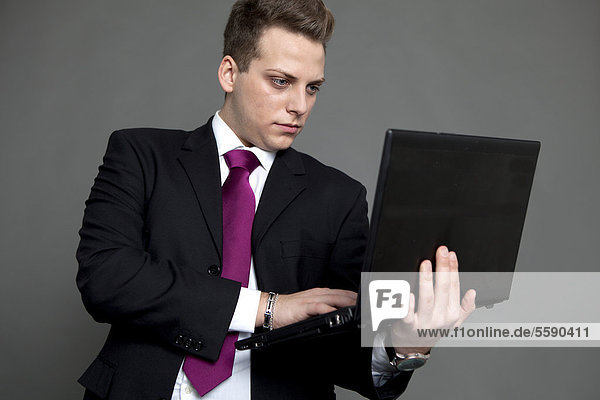 Junger Mann in Anzug und Krawatte  im Business-Look  mit Notebook
