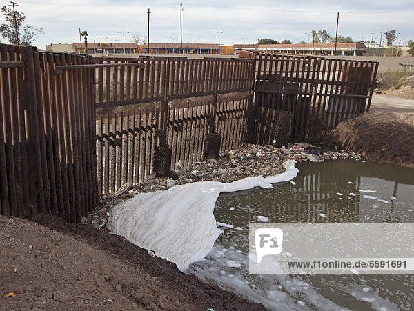 Der stark verschmutzte New River wie er die USA von Mexiko her erreicht die Umweltverschmutzung resultiert aus einer Mischung von ungeklärtem Abwasser landwirtschaftlichen Abflüssen und Gewerbemüll die Barriere im Fluss verhindert dass Migranten die USA über den Fluss erreichen um illegal in die USA einzureisen Calexico Kalifornien USA