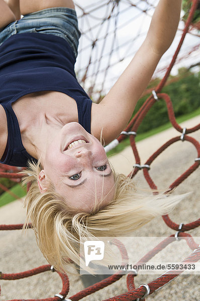 Deutschland  Nordrhein-Westfalen  Düsseldorf  Junge Frau am Klettergerüst auf dem Spielplatz  lächelnd