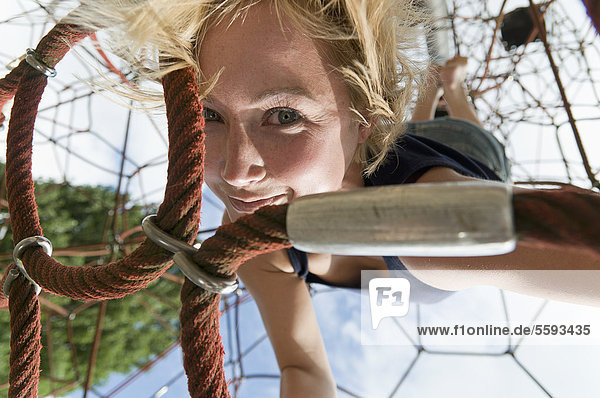 Deutschland  Nordrhein-Westfalen  Düsseldorf  Junge Frau am Klettergerüst im Spielplatz  lächelnd  Portrait