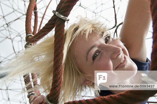Deutschland  Nordrhein-Westfalen  Düsseldorf  Junge Frau am Klettergerüst im Spielplatz  lächelnd  Portrait