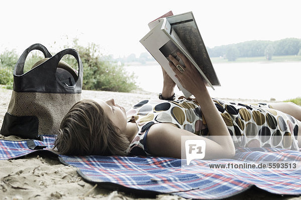 Young woman lying on blanket and reading book