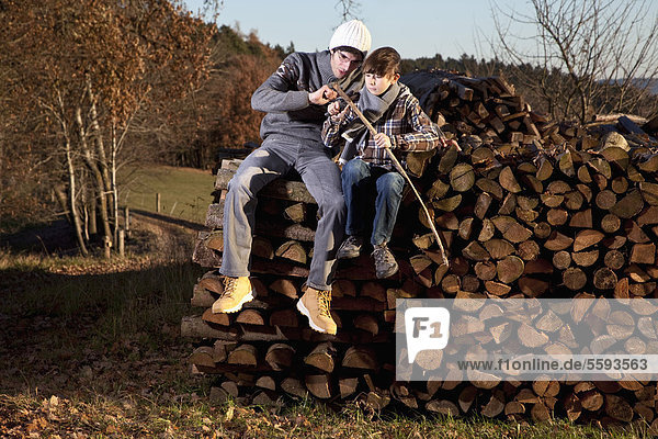 Deutschland  Bayern  Vater und Sohn sitzen auf Holz und Schneidstock