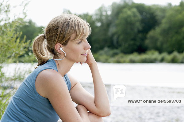 Mid adult woman listening to music near Isar river  smiling