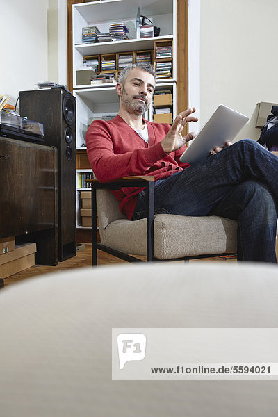 Erwachsener Mann sitzt auf Stuhl mit digitalem Tablett  lächelnd